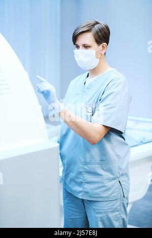 Junger MRT-MTRA mit Peelings und Maskendrücken auf dem MRT-Scannerfeld während der Arbeit in der Klinik Stockfoto