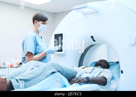 Junge kaukasische MRT-Technologie mit Maskendrücker auf dem Bedienfeld während der Vorbereitung des Patienten auf das Scannen Stockfoto