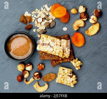 Arrangement von nützlichen Müsliriegel mit Müsli, Nüssen, getrockneten Aprikosen und einer Schüssel Honig auf schwarzem Stein Hintergrund. Draufsicht Stockfoto