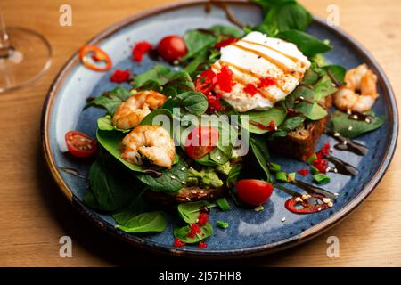 Das Buchweizenbrot wird mit einem pochierten Ei, einer in Scheiben geschnittenen Avocado, Garnelen, Tomaten und Salat geröstelt. Diätmenü. Flach liegend Stockfoto