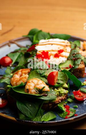 Das Buchweizenbrot wird mit einem pochierten Ei, einer in Scheiben geschnittenen Avocado, Garnelen, Tomaten und Salat geröstelt. Diätmenü. Flach liegend Stockfoto