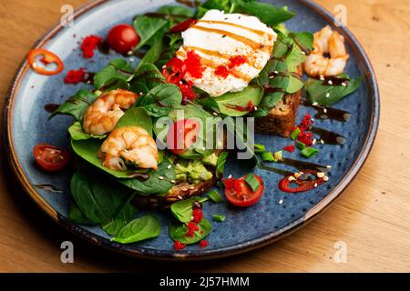 Das Buchweizenbrot wird mit einem pochierten Ei, einer in Scheiben geschnittenen Avocado, Garnelen, Tomaten und Salat geröstelt. Diätmenü. Flach liegend Stockfoto