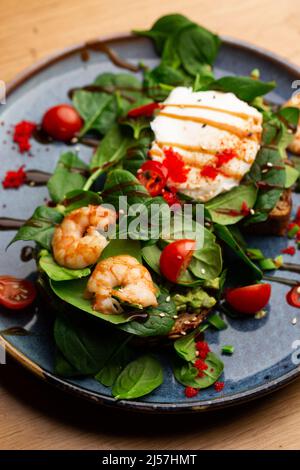 Das Buchweizenbrot wird mit einem pochierten Ei, einer in Scheiben geschnittenen Avocado, Garnelen, Tomaten und Salat geröstelt. Diätmenü. Flach liegend Stockfoto