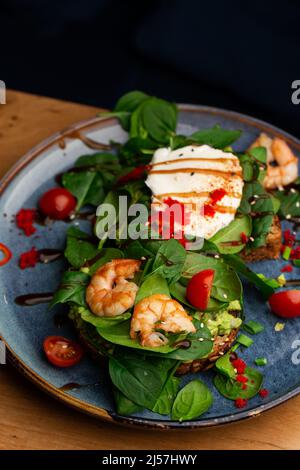 Das Buchweizenbrot wird mit einem pochierten Ei, einer in Scheiben geschnittenen Avocado, Garnelen, Tomaten und Salat geröstelt. Diätmenü. Flach liegend Stockfoto