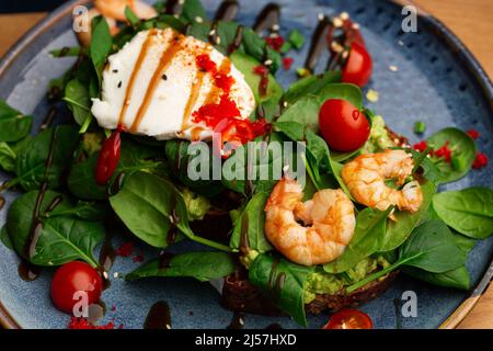 Das Buchweizenbrot wird mit einem pochierten Ei, einer in Scheiben geschnittenen Avocado, Garnelen, Tomaten und Salat geröstelt. Diätmenü. Flach liegend Stockfoto