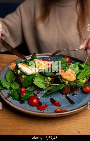 Das Buchweizenbrot wird mit einem pochierten Ei, einer in Scheiben geschnittenen Avocado, Garnelen, Tomaten und Salat geröstelt. Diätmenü. Flach liegend Stockfoto