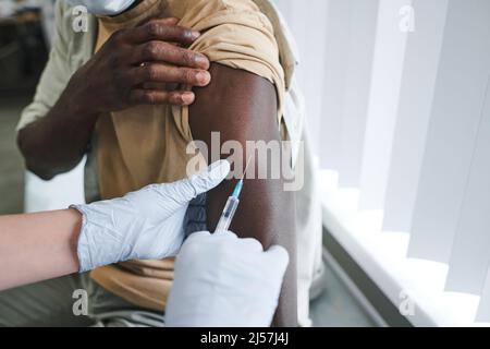 Nahaufnahme einer nicht erkennbaren Krankenschwester in Handschuhen, die die gefüllte Spritze halten und gleichzeitig die Injektionsstelle am Arm des Patienten bestimmen Stockfoto