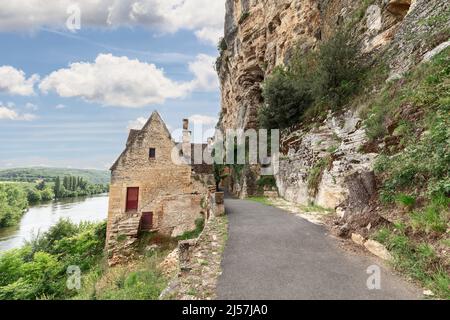 Abgeschiedenes Steinhaus auf der Straße entlang einer steilen Klippe auf einer Seite und voll fließendes Bett des Flusses Dordogne. Departement Dordogne, Region New Aquitaine, Frankreich Stockfoto