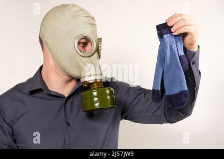 Ein Mann in einer Gasmaske hält schmutzig riechende Socken. Das Problem des unangenehmen Fußgeruchs bei Männern Stockfoto