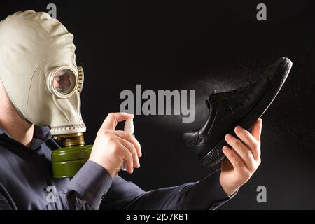 Ein Mann in einer Gasmaske behandelt seine Schuhe mit einem Duftspray, dem Problem des unangenehmen Geruchs an Füßen und Schuhen Stockfoto