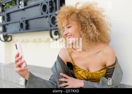Portrait glückliche lateinische junge Frau mit lockigen blonden Haaren mit Handy Stockfoto