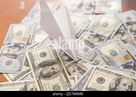 origami-Flugzeug landet auf einem Stapel von Banknoten aus dem US-Dollar. Stockfoto