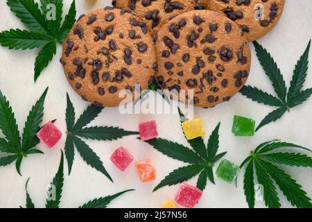 Amerikanische Cookies mit Cannabisextrakt. Süßigkeiten mit CBD-Öl. Marihuana Blätter auf weißem Hintergrund. Draufsicht, flach liegend. Stockfoto