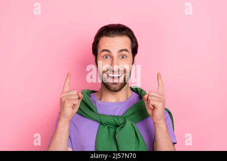 Foto von beeindruckt Millennial Brunet Mann zeigen bis tragen violette T-Shirt isoliert auf rosa Hintergrund Stockfoto