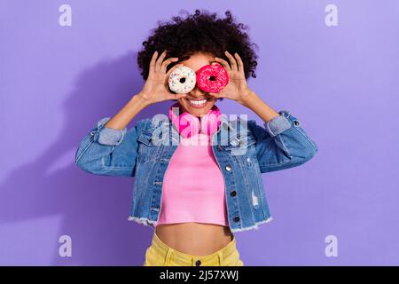 Portrait von schönen trendigen fröhlich wellig-haarige Mädchen hält Donuts wie Gläser isoliert über hellen violett lila Farbe Hintergrund Stockfoto