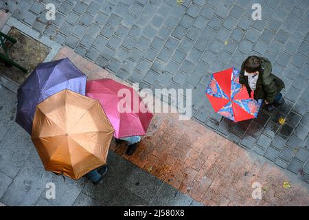 Gruppen von Menschen, die sich an einem regnerischen Tag in Madrid, Spanien, unter Regenschirmen unterhalten. Stockfoto