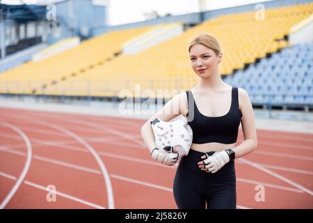 Lächelnde Frau in Sportswear, die Sporthelm hält und wegschaut Stockfoto
