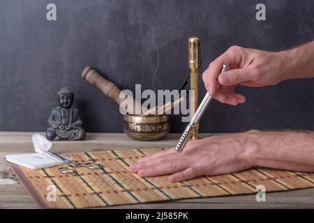 Moxibustherapie - traditionelle Chinesische Medizin. Platzierung des brennenden Moxa-Sticks auf der Hand. Stockfoto