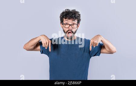 Ein hübscher Mann zeigte nach unten, ein überraschender Mann zeigte mit den Fingern nach unten, ein erstaunter junger Mann zeigte nach unten Stockfoto