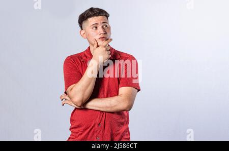 Junger Mann wundert sich mit der Hand auf dem Kinn auf einem isolierten Hintergrund, ein Mann denkt mit der Hand auf dem Kinn Stockfoto