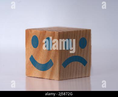 Foto eines Holzwürfels mit glücklichen und traurigen Gesichtsausdrücken als Symbol für instat-Persönlichkeitsverschiebungen. Konzept von bipolar , unipolar und borderline. Stockfoto