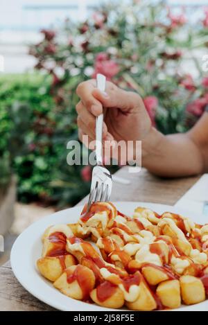 Nahaufnahme eines Mannes, der im Begriff ist, typische spanische Patatas-Bravas zu essen, frittierte Kartoffeln mit einer heißen Sauce, die an einem Restauranttisch im Freien sitzen Stockfoto