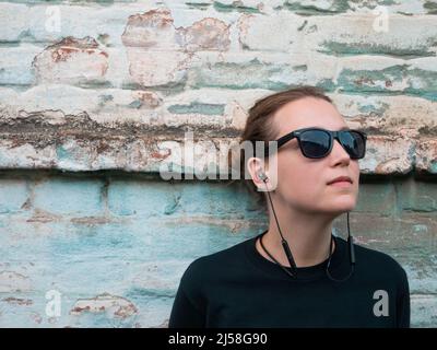 Porträt eines jungen attraktiven Mädchen in schwarzem T-Shirt und Sonnenbrille im Rock-Stil auf städtischen Hintergrund Musik mit Kopfhörern hören. Hipster in wir Stockfoto