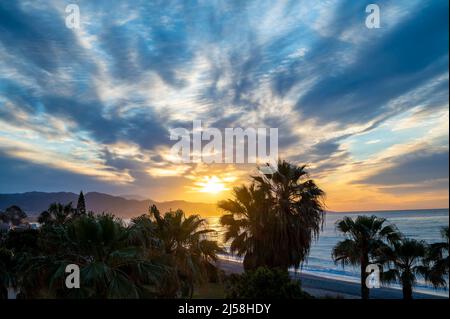 Sonnenaufgang über Meerwasser und Palmen in Torrox Costa, Costa del Sol, kleiner touristischer Ort zwischen Malaga und Nerja, Andalusien, Spanien Stockfoto