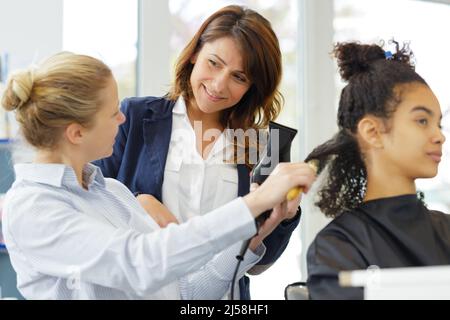 Friseurlehrling bügeln die Haare des Kunden Stockfoto