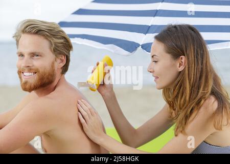 Freundin, die am Strand Sonnencreme auf ihren Freund auftragen Stockfoto