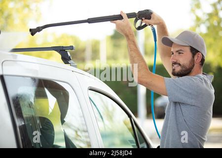 Ein grauer Mann wäscht sein Auto bei einer Autowäsche Stockfoto