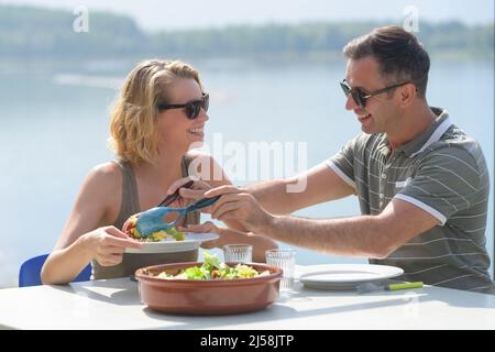 Junges Paar beim Mittagessen am See Stockfoto