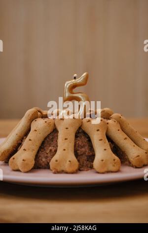 Geburtstagsfeier für Haustier. Kuchen aus Pastete und Keksen in Form von Knochen. Die goldene Kerze in Form der Zahl 5 wird so angezündet, dass der Hund oder die Katze ha Stockfoto