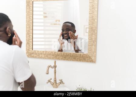 Schwarzer glücklicher Mann wäscht sein Gesicht im Badezimmer. Tägliche Routine. Stockfoto