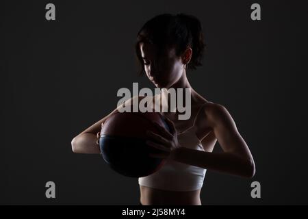 Teenager Mädchen mit Basketball. Seitlich beleuchtetes Studioporträt vor dunklem Hintergrund. Stockfoto