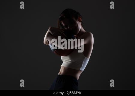 Teenager Mädchen mit Basketball. Seitlich beleuchtetes Studioporträt vor dunklem Hintergrund. Stockfoto