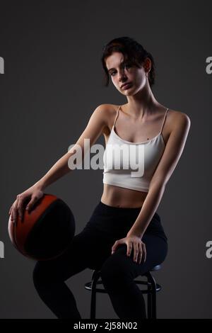 Teenager Mädchen mit Basketball. Seitlich beleuchtetes Studioporträt vor dunklem Hintergrund. Stockfoto