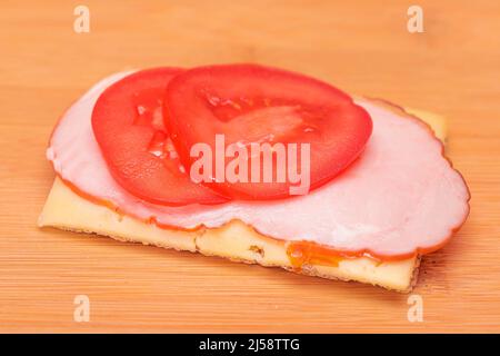 Vollkorn-Knäckebrot mit Tomaten, Schinken und Käse auf Bamboo Cutting Board. Einfaches Frühstück. Schnelle und gesunde Sandwiches. Knäckebrot mit leckerer Füllung. Gesunder Ernährungs-Snack Stockfoto