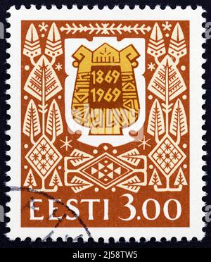 ESTLAND - UM 1994: Eine in Estland gedruckte Briefmarke, die zum 125.. Jahrestag des estnischen Liedfestivals ausgegeben wurde, zeigt das Liedfest-Abzeichen aus dem Jahr 1969. Stockfoto