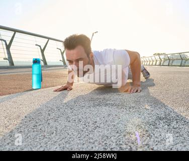 Kaukasischer Mann mittleren Alters, Sportler und Sportler, der Liegestützübungen während des Outdoor-Trainings auf der gläsernen Stadtbrücke im Morgengrauen durchführt. Sport, Fitness, aktiv Stockfoto