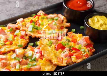 Fritten mit Mais, Schinkenpfeffer und Zwiebel mit Saucen aus der Nähe auf einem Teller auf dem Tisch serviert. Horizontal Stockfoto