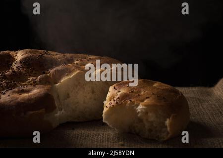 Nahaufnahme eines handgeteilten Ramadan-Pitabrabrotes auf Jute-Hintergrund mit Rauch Stockfoto