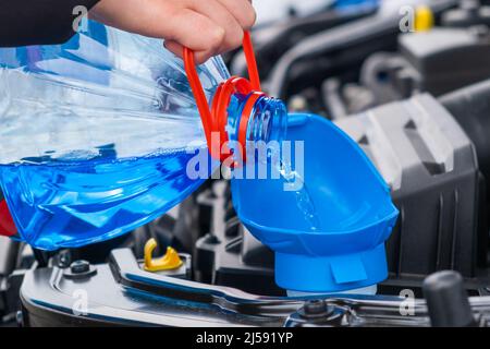 Nahaufnahme des Fahrers, der blaue, nicht gefrierende Scheibenwaschflüssigkeit in den Tank des Fahrzeugs gießt. Stockfoto