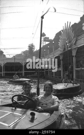 1950s, eine historische Mutter mit ihrem jungen Sohn, die in einem Holzboot auf dem Bootspool im Dreamland Pleasure Park in Margate, Kent, England, sitzt. Der See wurde 1937 eröffnet. Stockfoto