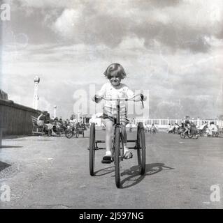 1960, Historcal, ein kleines Mädchen auf einem Mietdreirad auf einem breiten Ebenen Platz an einer Strandpromenade, England, Großbritannien. Stockfoto