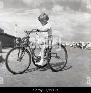 1960, Historcal, ein kleines Mädchen, das auf einem großen, Ebenen Platz an einer Strandpromenade ein Mietdreirad reitet, England, Großbritannien. Stockfoto