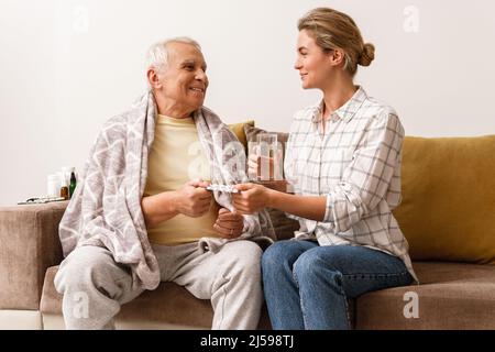 Die junge Frau gibt ihrem kranken älteren Großvater zu Hause Medikamente Stockfoto