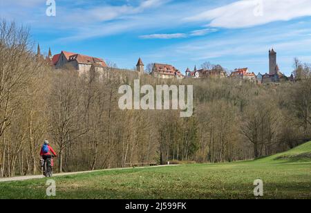 Nette Stadtfrau auf einer Radtour auf der berühmten deutschen Schlossroute, unterhalb der mittelalterlichen Skyline von Rothenburg ob der Tauber, Bayern, Deutschland Stockfoto