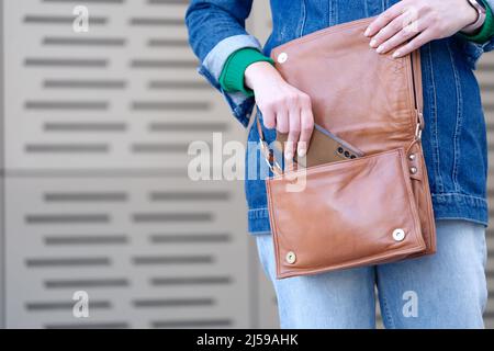 Frau, die das Mobiltelefon in eine braune Lederhandtasche in Nahaufnahme legt Stockfoto