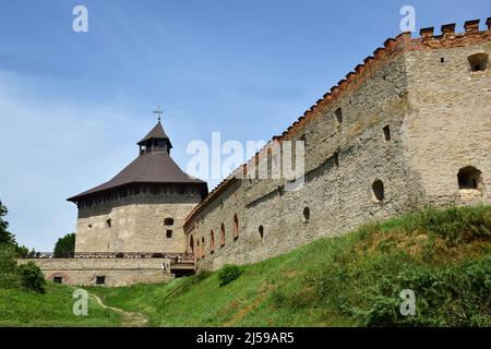 Eine mächtige Steinmauer einer mittelalterlichen Festung mit vielen Schlupflöchern und Schießscharten. In der Ferne ein großer Turm mit Dach Stockfoto